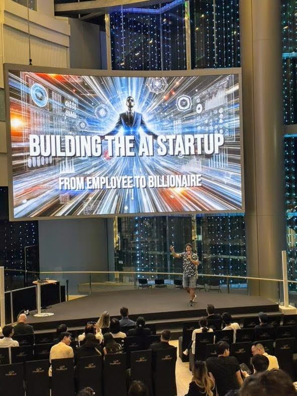 Daniel Duma on a large stage in Bangkok under a screen reading “Building the AI startup: from employee to billionaire”